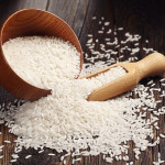 Rice in brown bowl and scattered near on dark wooden table